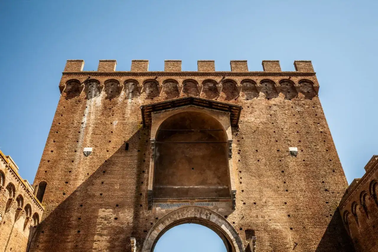 Imponente porta romana in mattoni con merlature e un arco maestoso.