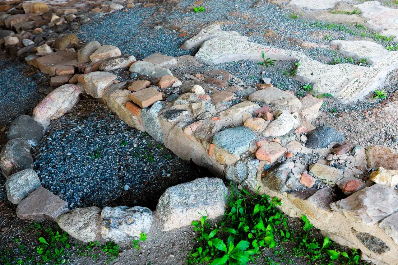 Resti archeologici a Bova Marina: un muro di pietre e mattoni antichi, con frammenti di mosaico, circonda un'area di ghiaia scura.
