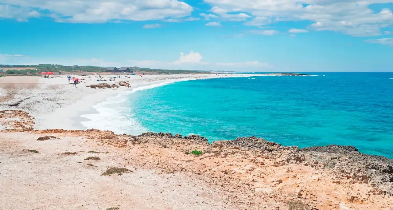 Spiaggia di vetro in Sardegna, con sabbia bianca, mare turchese e rocce rossastre.