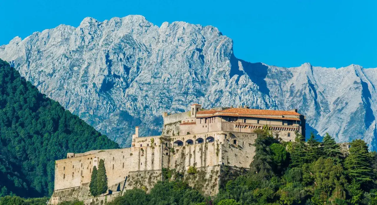 Fortezza arroccata su una collina verde, con imponenti montagne sullo sfondo. C'è massa cosa vedere in questo paesaggio mozzafiato.