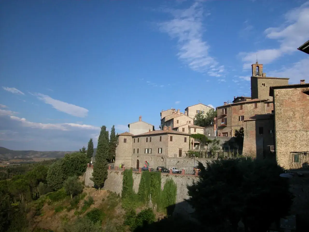 Panicale, borgo medievale in Umbria, si erge su una collina sotto un cielo azzurro con nuvole bianche.