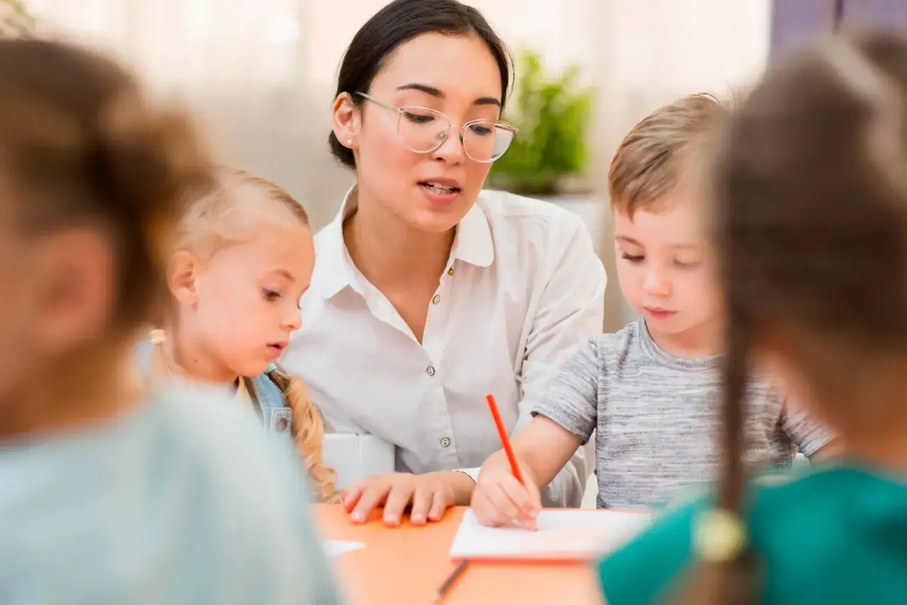 Maestra con occhiali, un assistente alla comunicazione, insegna a bambini a disegnare.