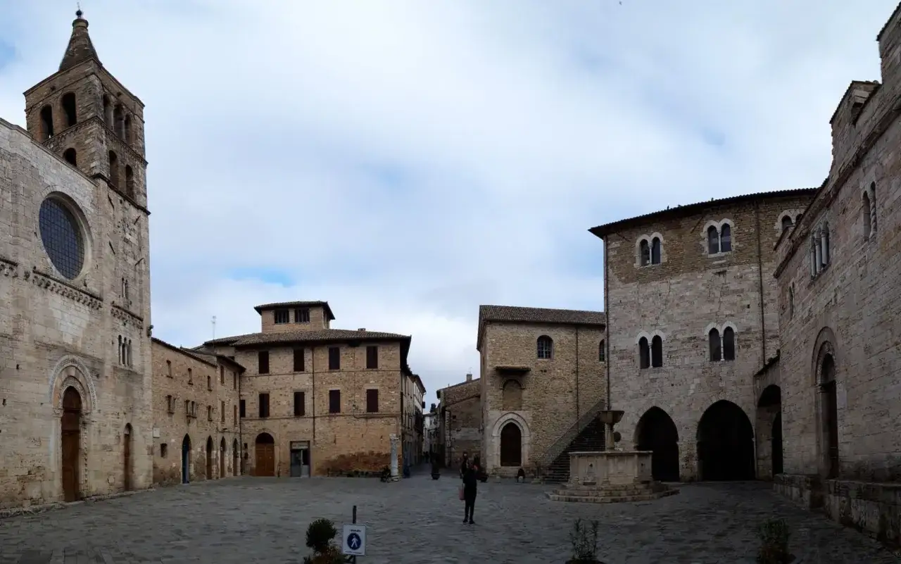Piazza medievale a Bevagna, Umbria, con campanile romanico, palazzi in pietra e una fontana.