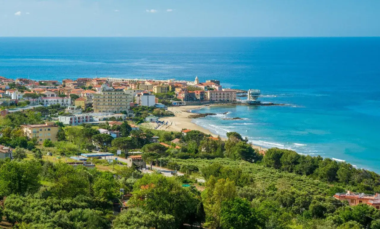Vista panoramica di una cittadina costiera con edifici colorati, una spiaggia sabbiosa e il mare blu intenso. Questo è un assaggio di dove si trova Pollica, un gioiello del Cilento.