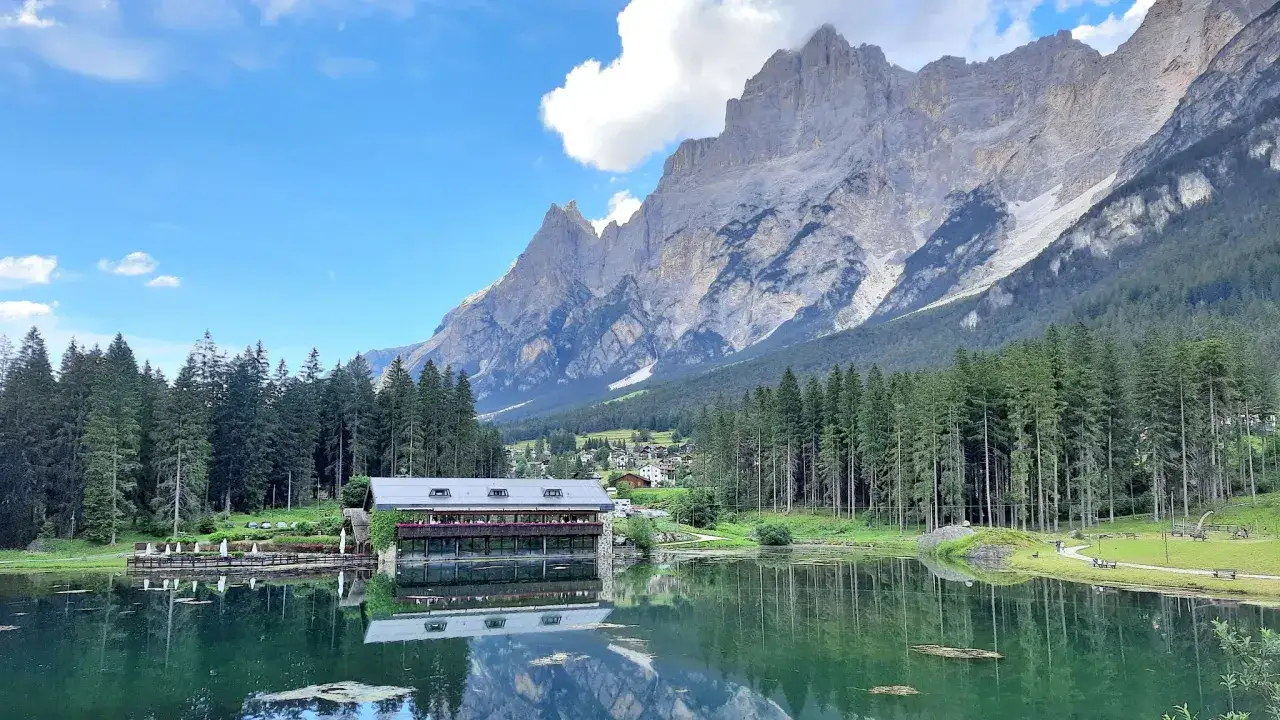 Lago alpino con rifugio e montagne maestose, ideale per il trekking in Cadore. Riflessi sull'acqua cristallina.