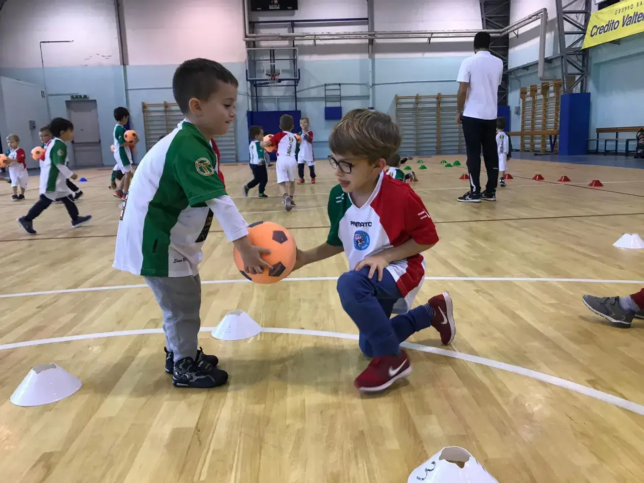 Bambini giocano a pallone durante l'educazione fisica scuola primaria. Un bambino porge la palla all'altro.
