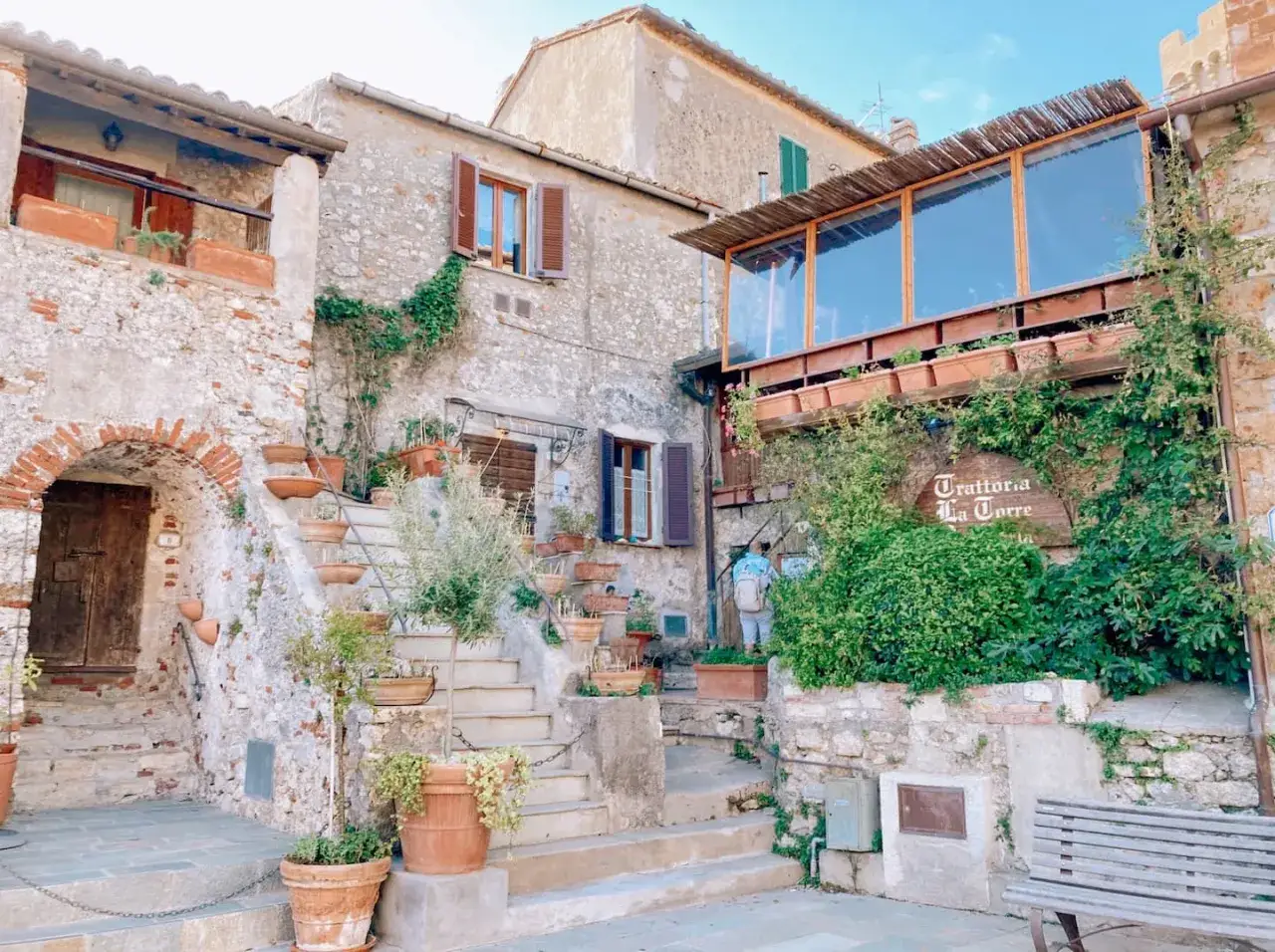 Un caparbio paese con scale di pietra, vasi di terracotta e un'insegna di trattoria.