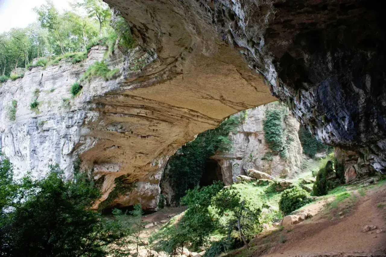 Il ponte di Veja, una meraviglia naturale scavata nella roccia, offre uno scorcio su un'antica grotta circondata da vegetazione lussureggiante.