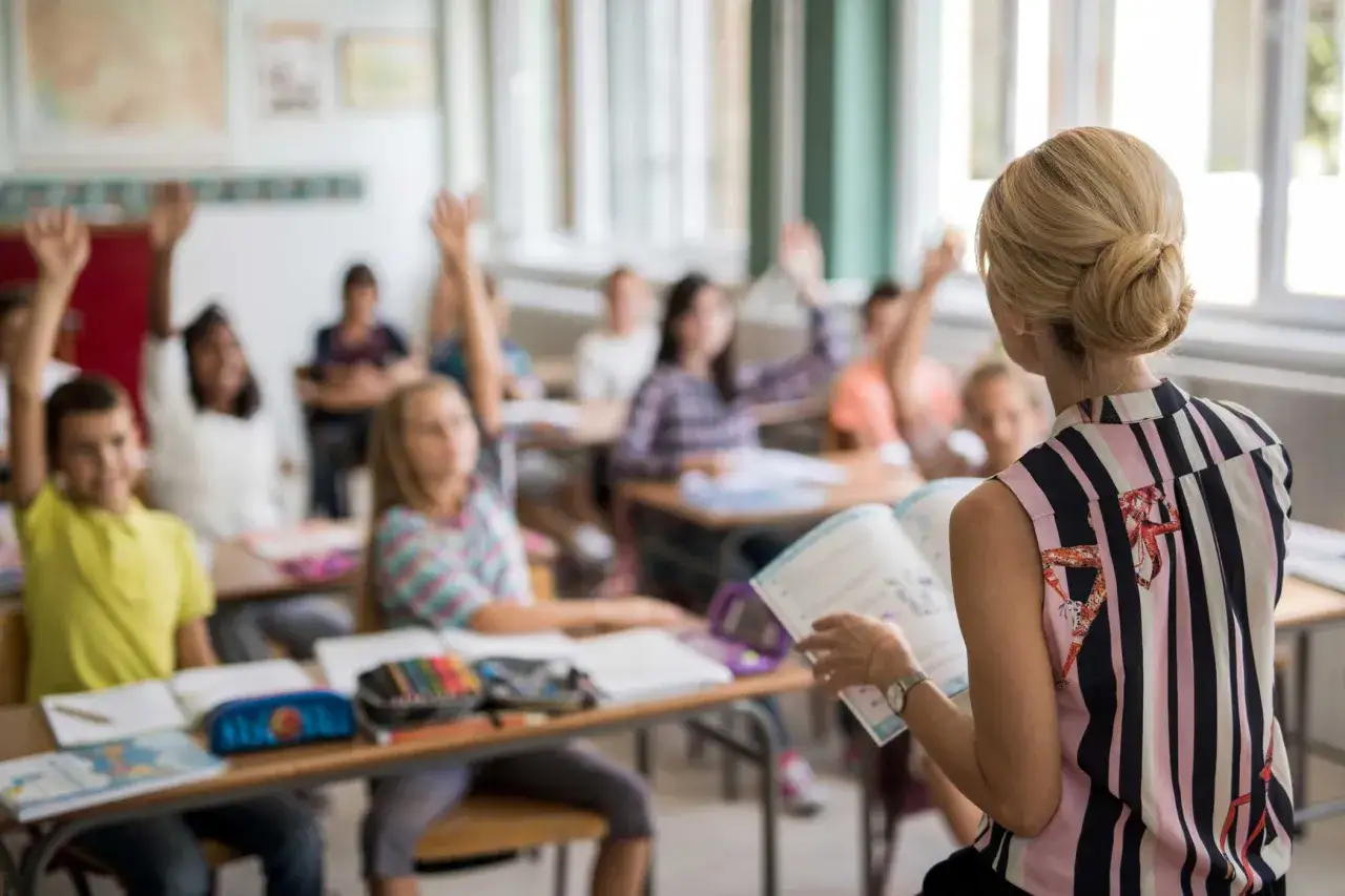 Classe con alunni che alzano la mano, insegnante legge. Il sfp significato università è un percorso di studi che porta a nuove conoscenze.
