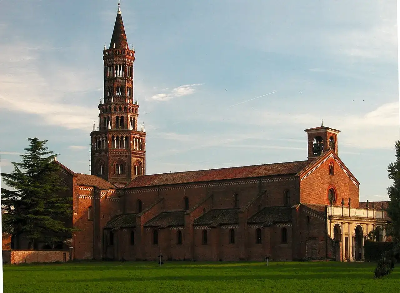 La maestosa abbazia di Chiaravalle, con la sua torre campanaria slanciata e la facciata in mattoni rossi, si staglia contro un cielo azzurro.