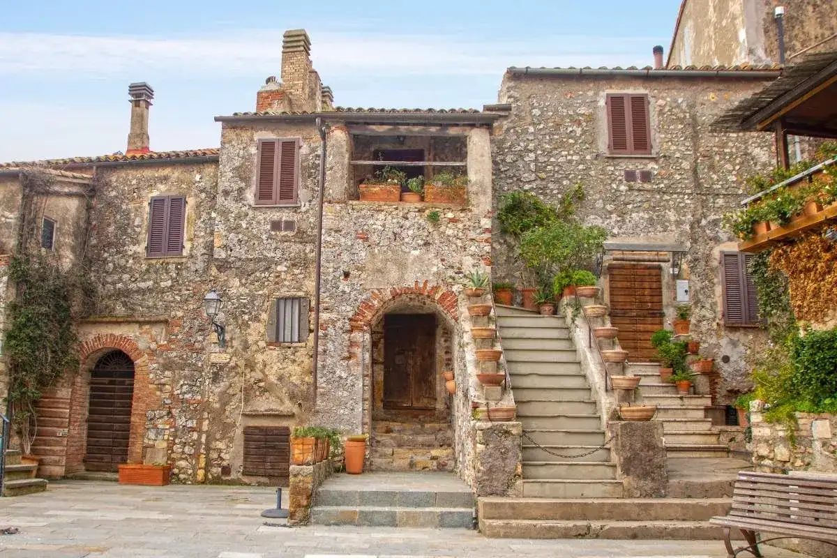 Antica piazza in uno dei borghi toscana, con case in pietra, scale fiorite e un portico accogliente.
