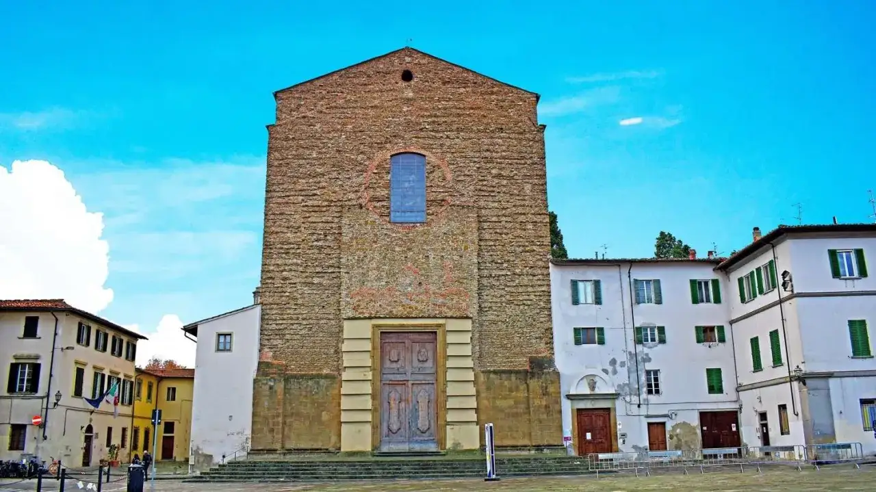 La facciata in pietra grezza di Santa Maria del Carmine domina la piazza, con un grande portale in legno e un rosone blu.