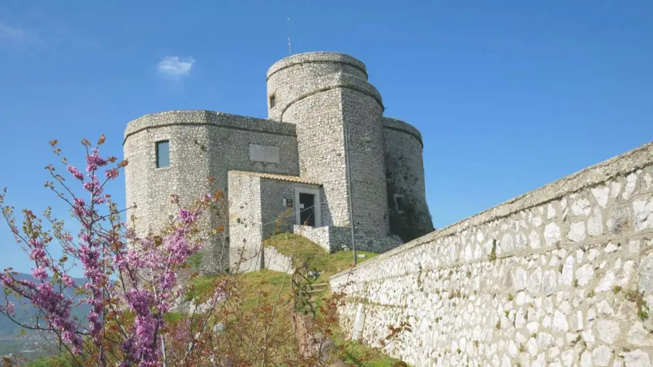 Castello di Montesarchio, Benevento, imponente fortezza in pietra con torri circolari, circondata da mura antiche e fioriture primaverili.